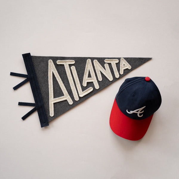 Baseball cap with red brim and blue top next to a black flag with 'Atlanta' written on it on a light gray background