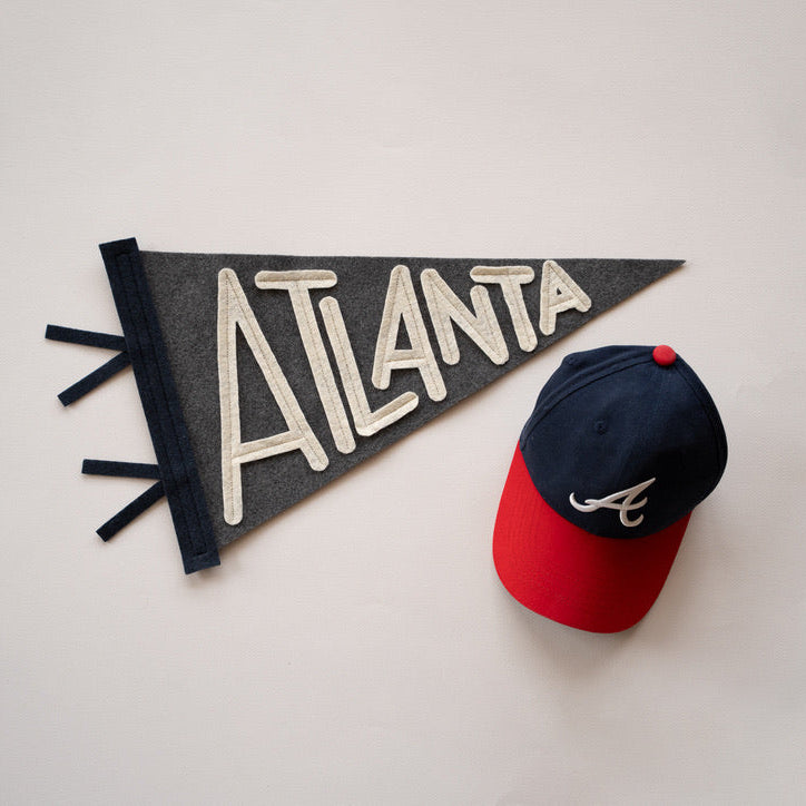 Baseball cap with red brim and blue top next to a black flag with 'Atlanta' written on it on a light gray background